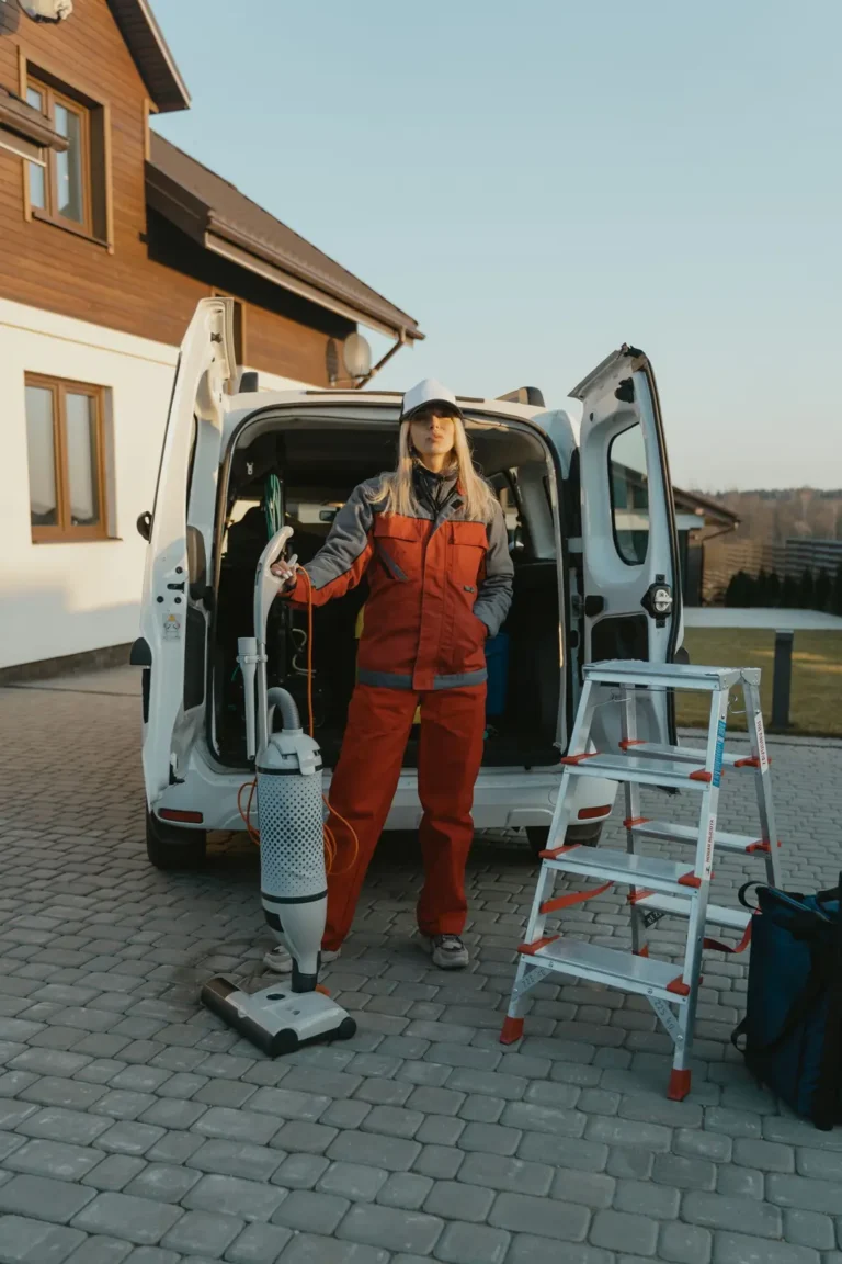 House cleaner with equipment beside a service van outside a home