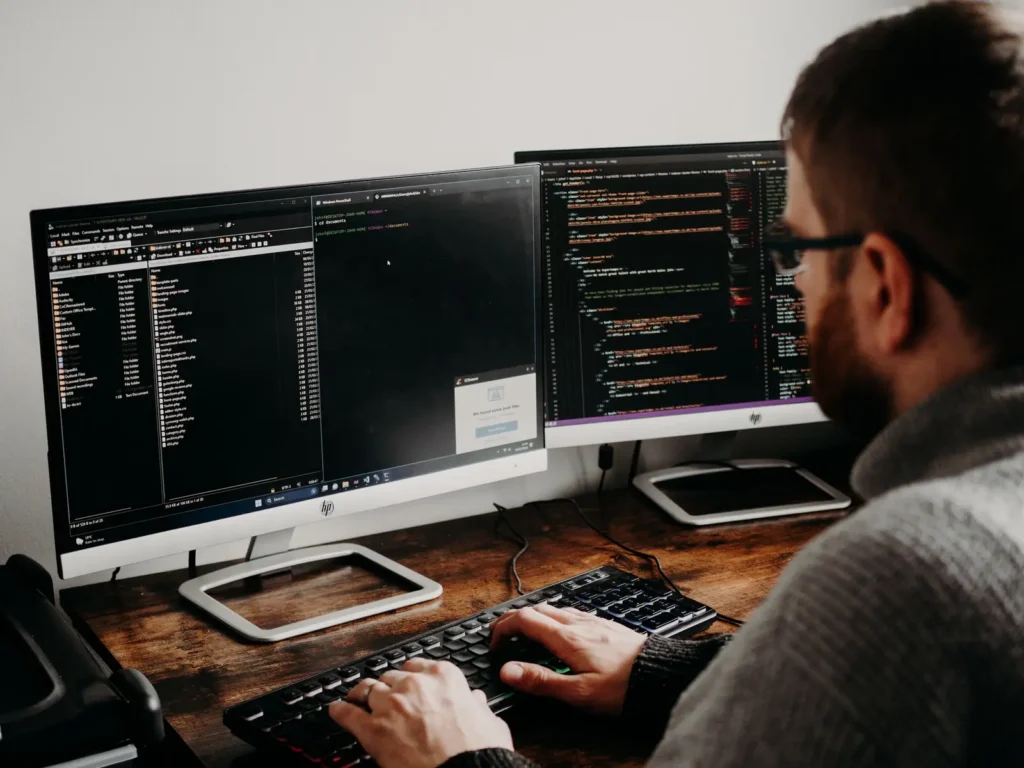 Developer typing code on dual monitors at a wooden desk