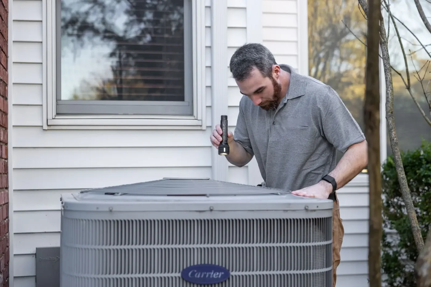 HVAC technician working on an outdoor air conditioning unit beside a home
