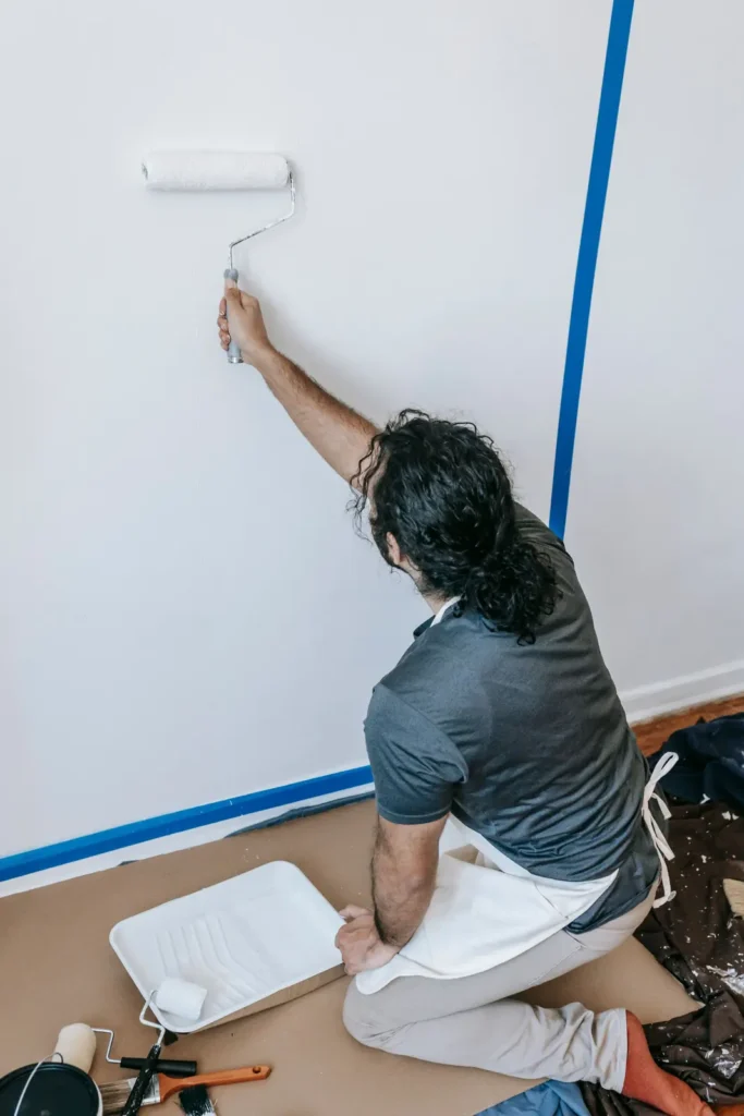 Painter rolling a wall beside fresh painter's tape