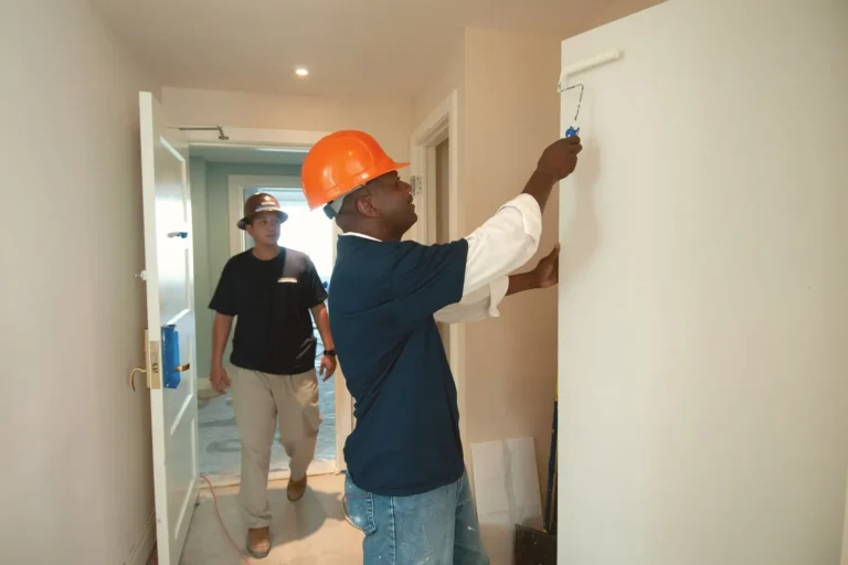 Painter rolling paint onto an interior wall while a coworker watches
