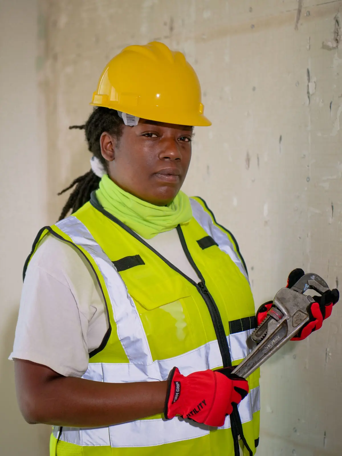 Plumber in a hard hat and safety vest holding a pipe wrench